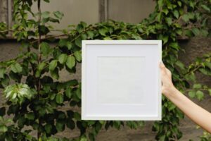 Empty white frame held outdoors among lush leaves, ready for your photo.